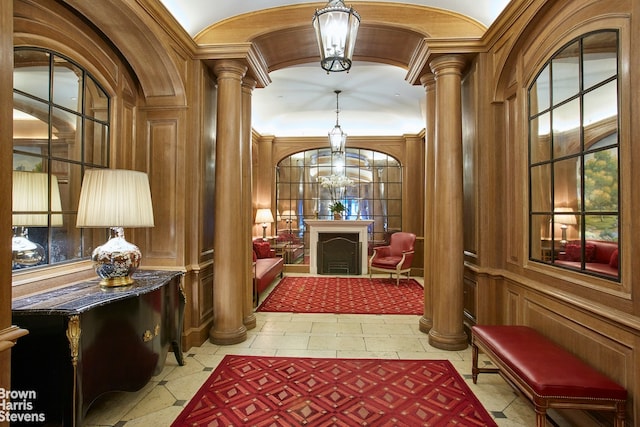 hallway featuring decorative columns, wooden walls, and an inviting chandelier