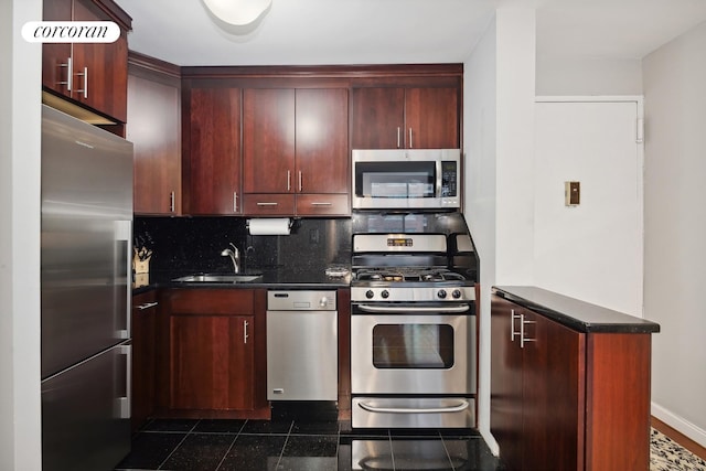 kitchen featuring backsplash, a sink, appliances with stainless steel finishes, dark countertops, and reddish brown cabinets