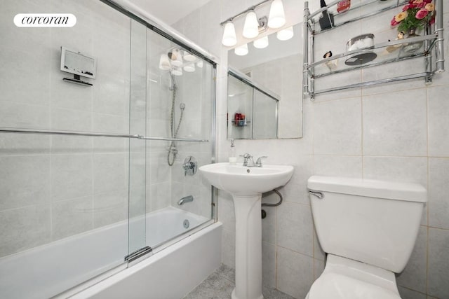 full bathroom with tile walls, sink, combined bath / shower with glass door, and toilet