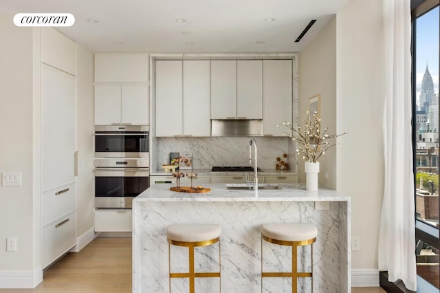 kitchen featuring a breakfast bar area, light hardwood / wood-style flooring, white cabinetry, backsplash, and stainless steel double oven