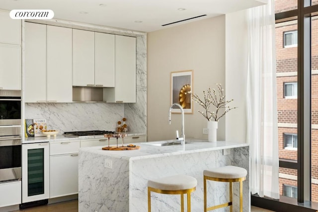 kitchen featuring stainless steel gas cooktop, backsplash, white cabinets, a healthy amount of sunlight, and beverage cooler