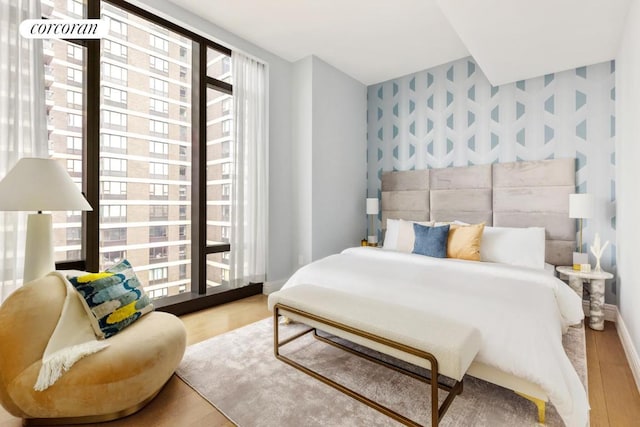 bedroom featuring an accent wall, light wood-style floors, baseboards, and wallpapered walls