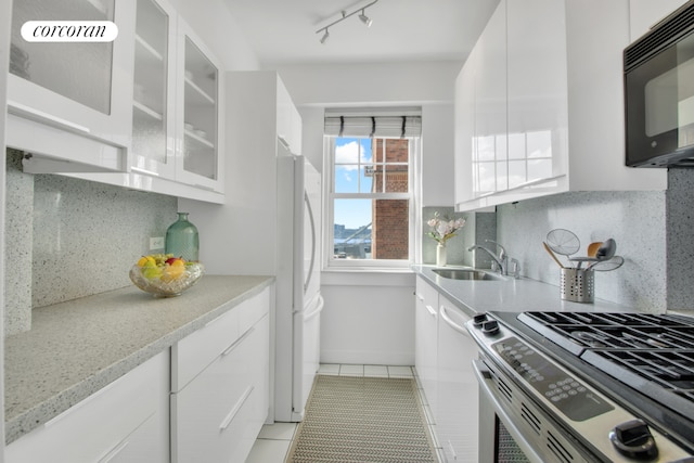 kitchen with sink, stainless steel gas stove, white cabinetry, light tile patterned floors, and white fridge