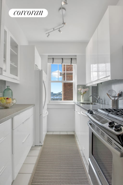 kitchen with light tile patterned floors, white refrigerator, stainless steel range, white cabinets, and decorative backsplash