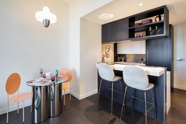 kitchen featuring a kitchen bar, light countertops, decorative backsplash, dark wood-style floors, and modern cabinets