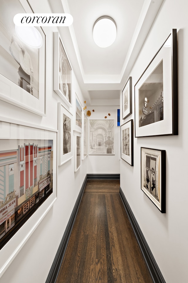 hall featuring dark wood-style flooring, a raised ceiling, and baseboards