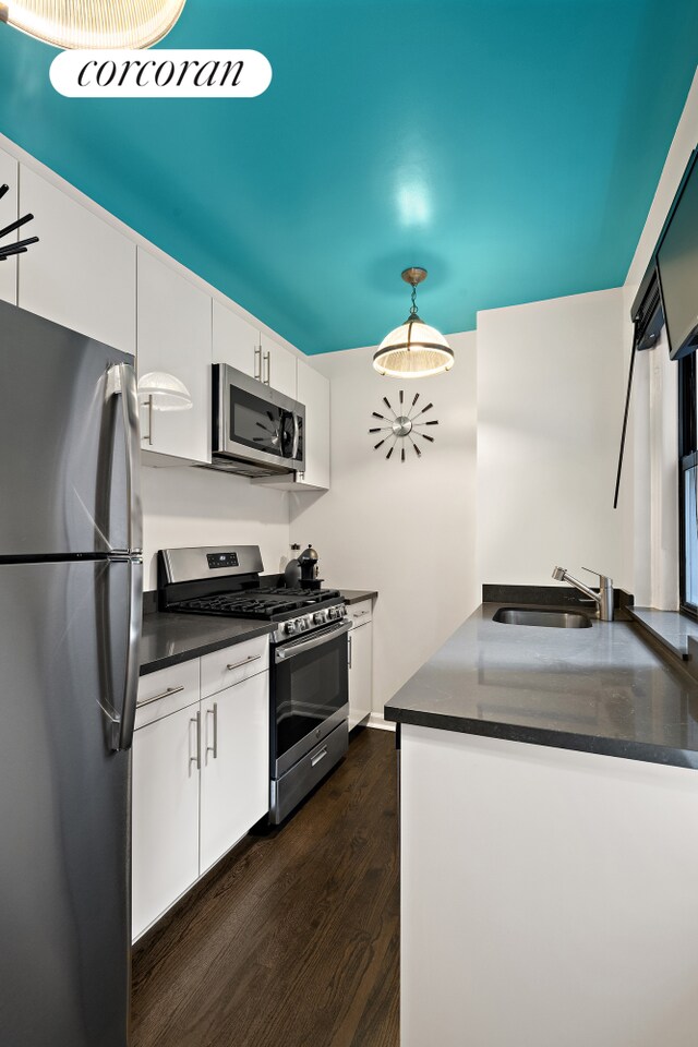 kitchen featuring pendant lighting, sink, appliances with stainless steel finishes, dark hardwood / wood-style floors, and white cabinets