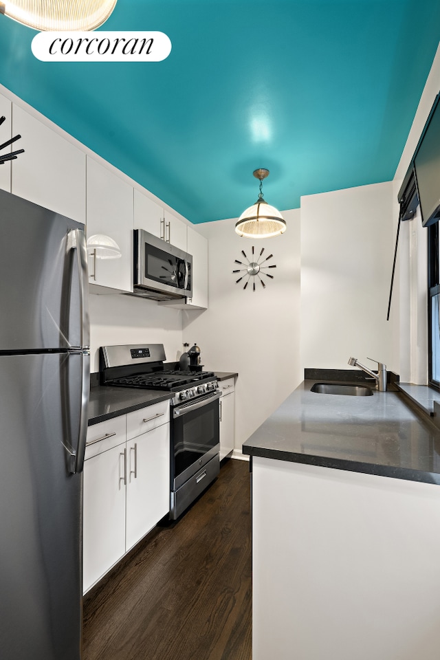 kitchen with dark wood finished floors, dark countertops, stainless steel appliances, white cabinetry, and a sink