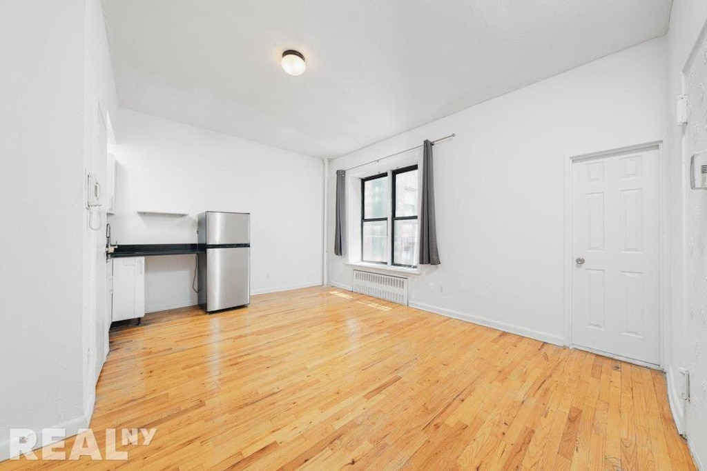 empty room with radiator heating unit and light hardwood / wood-style flooring