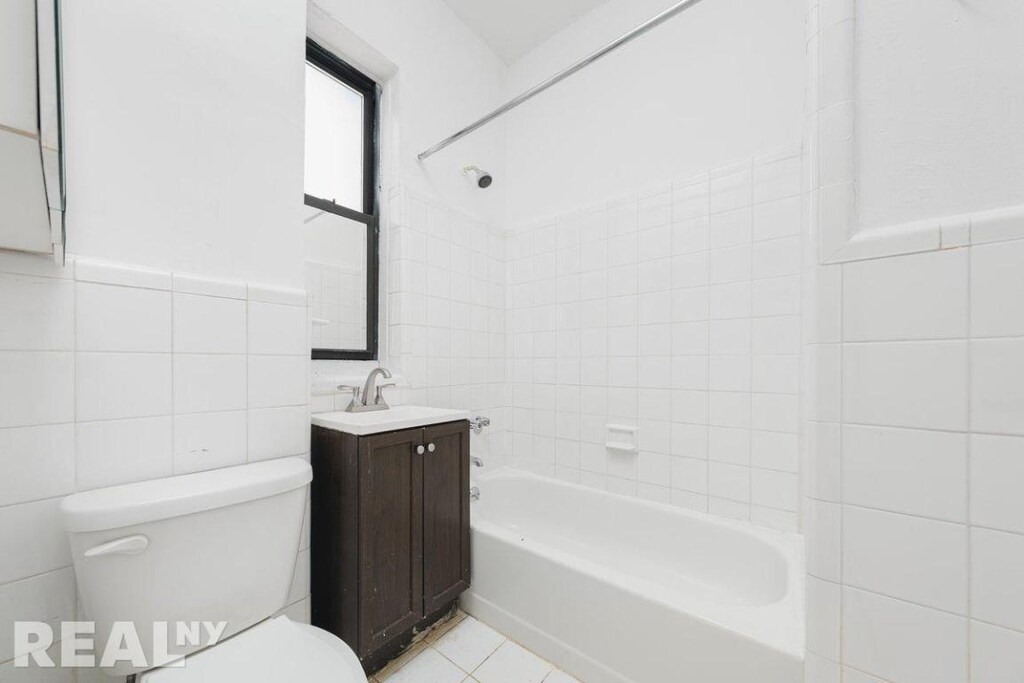 full bathroom with toilet, vanity, tile walls, tiled shower / bath, and tile patterned floors