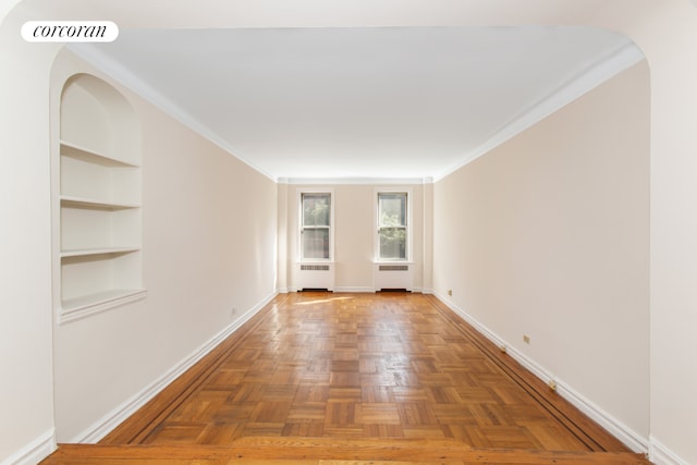 spare room featuring dark parquet flooring, crown molding, radiator heating unit, and built in features