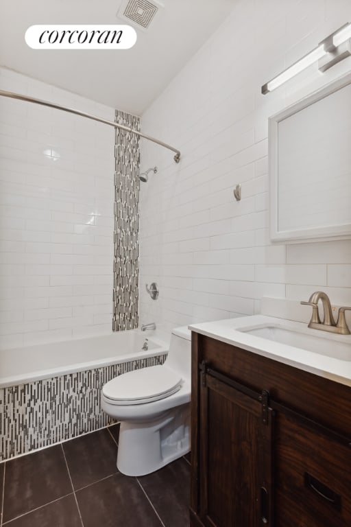 full bathroom with tile walls, tiled shower / bath combo, vanity, toilet, and tile patterned floors