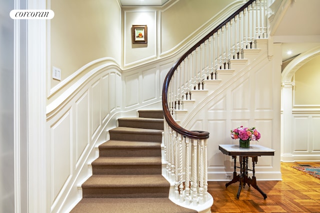 stairs featuring arched walkways, a decorative wall, and wood finished floors