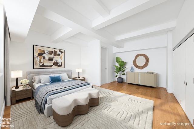 bedroom featuring light wood-style floors, beam ceiling, a closet, and baseboards