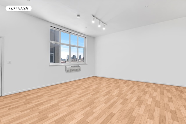 spare room featuring track lighting, a wall unit AC, and light hardwood / wood-style flooring