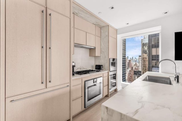 kitchen with light stone counters, cream cabinets, stainless steel appliances, and sink