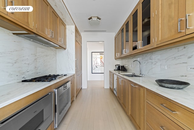 kitchen featuring stainless steel gas stovetop, sink, light stone counters, wall oven, and light wood-type flooring