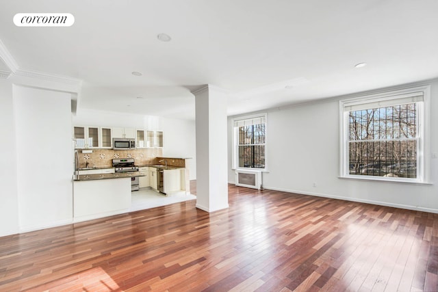 unfurnished living room featuring wood-type flooring, visible vents, ornate columns, ornamental molding, and baseboards