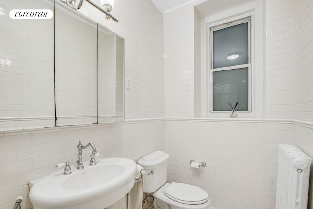 half bathroom featuring toilet, a sink, tile walls, and radiator heating unit