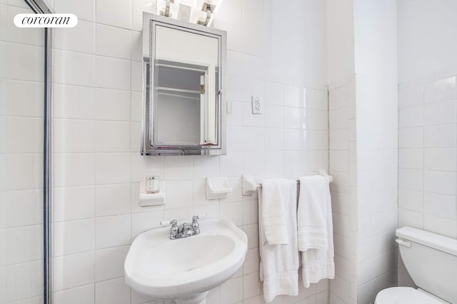 bathroom with toilet, a sink, and tile walls