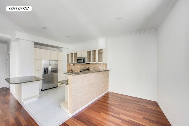 kitchen featuring a peninsula, appliances with stainless steel finishes, glass insert cabinets, and visible vents