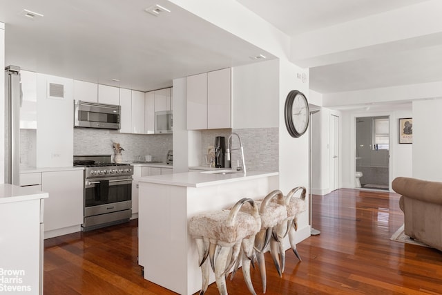 kitchen with white cabinets, appliances with stainless steel finishes, tasteful backsplash, sink, and kitchen peninsula