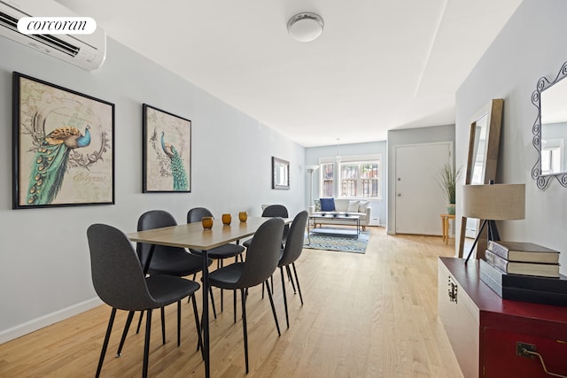 dining area featuring baseboards, light wood-style floors, and an AC wall unit