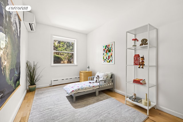 bedroom featuring an AC wall unit, wood finished floors, baseboards, and baseboard heating