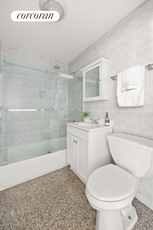 full bathroom featuring bath / shower combo with glass door, tile walls, toilet, and vanity