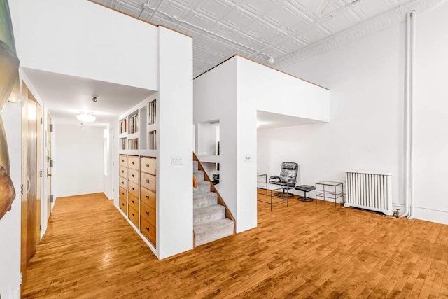 hall with a towering ceiling, hardwood / wood-style floors, and radiator heating unit