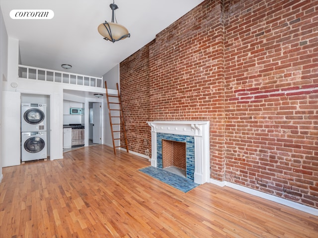 54 W 71st Street Building, New York City, NY 10023 - unfurnished living room featuring stacked washing machine and dryer, brick wall, hardwood / wood-style floors, and a fireplace with flush hearth