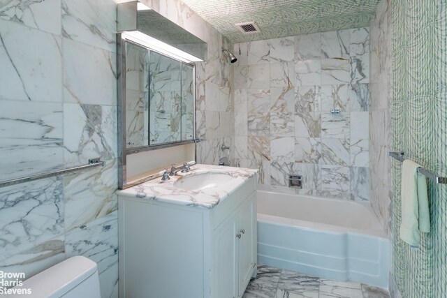 full bathroom with vanity, tile walls, toilet, and tiled shower / bath