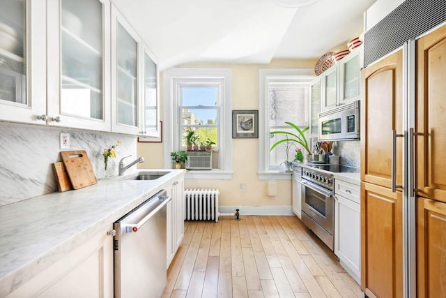 kitchen with radiator, white cabinetry, sink, premium appliances, and light stone countertops