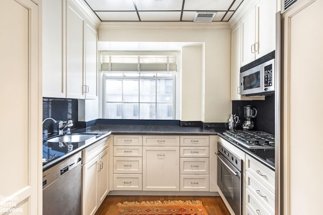 kitchen featuring stainless steel appliances, dark countertops, decorative backsplash, white cabinetry, and a sink