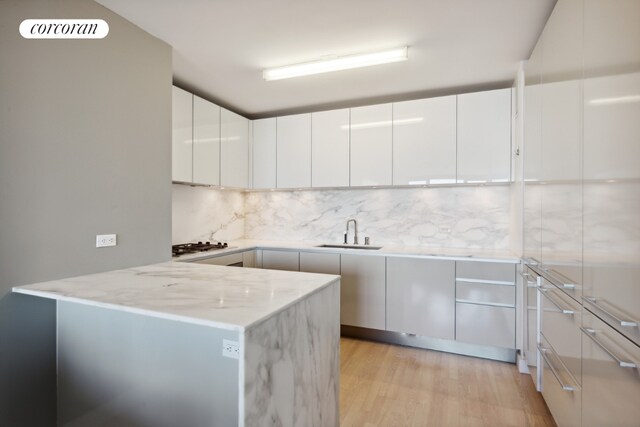 kitchen featuring sink, light hardwood / wood-style flooring, light stone countertops, white cabinets, and decorative backsplash