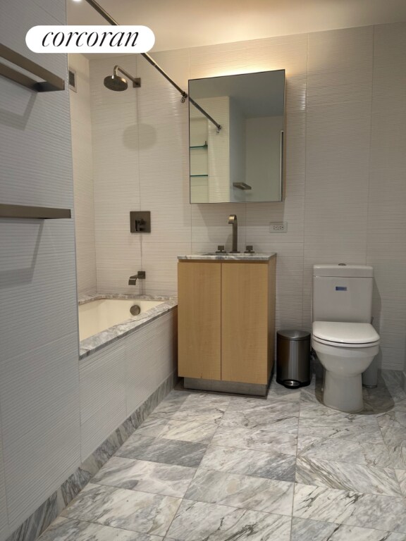 full bathroom featuring vanity, tile walls, toilet, and tiled shower / bath