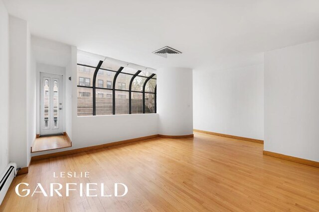 spare room featuring a baseboard heating unit, visible vents, baseboards, and wood finished floors