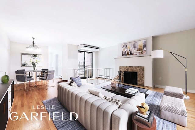 living area featuring a baseboard radiator, a notable chandelier, a premium fireplace, baseboards, and light wood finished floors