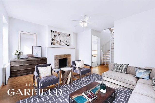 living room with ceiling fan, a premium fireplace, stairway, and wood finished floors