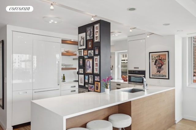 kitchen featuring a breakfast bar, white cabinetry, sink, stainless steel oven, and kitchen peninsula