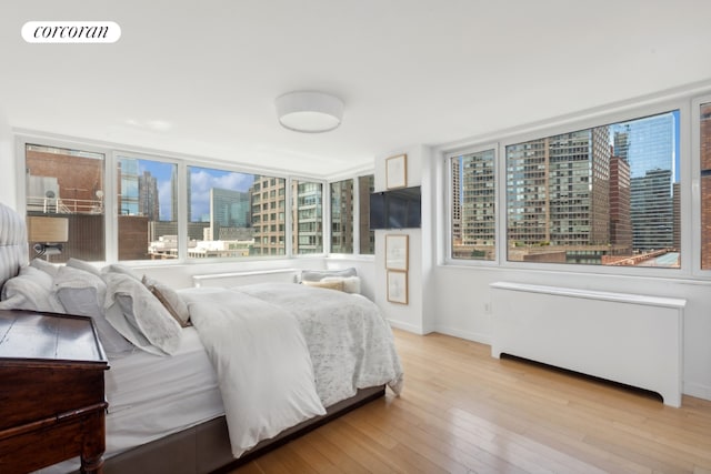 bedroom featuring light wood-style floors, radiator heating unit, visible vents, and baseboards