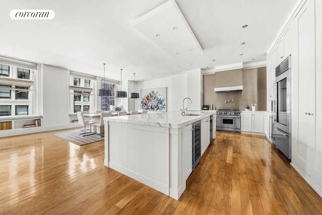 kitchen featuring white cabinets, a kitchen island with sink, a sink, and high quality appliances