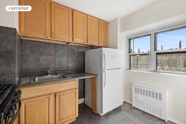 kitchen with a sink, range with gas stovetop, backsplash, radiator heating unit, and freestanding refrigerator