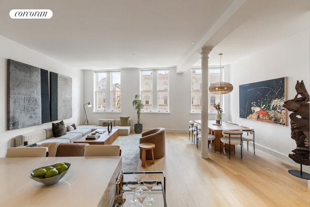 living area with baseboards, light wood finished floors, visible vents, and ornate columns