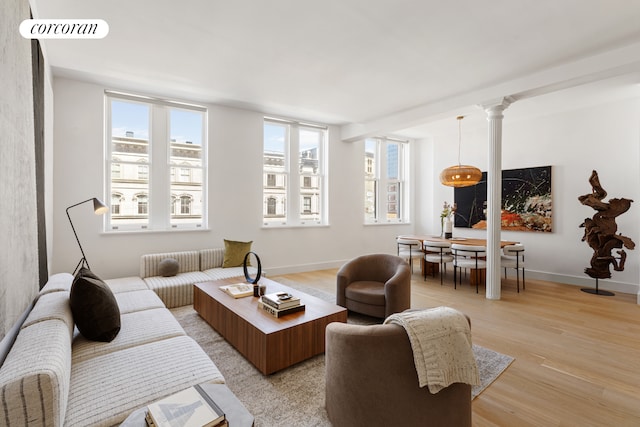 living area featuring light wood-style floors, ornate columns, visible vents, and baseboards