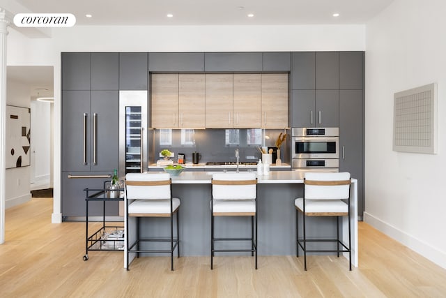 kitchen with light wood finished floors, visible vents, decorative backsplash, an island with sink, and gray cabinetry