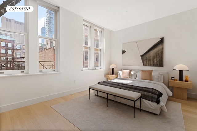 bedroom with a view of city, wood finished floors, and baseboards