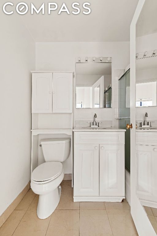 bathroom with a shower with shower door, tile patterned floors, vanity, and toilet