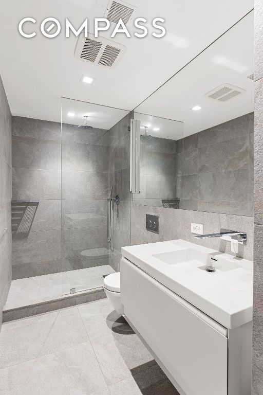 bathroom with tiled shower, toilet, tile walls, vanity, and backsplash