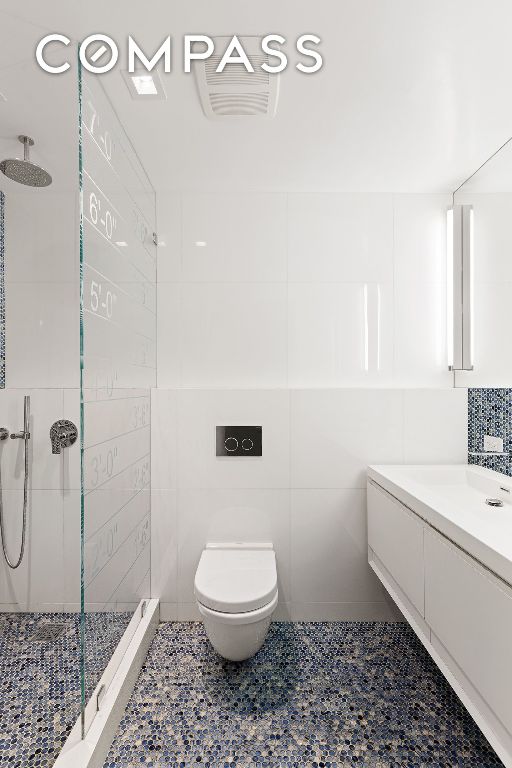 bathroom with vanity, a tile shower, tile walls, and toilet